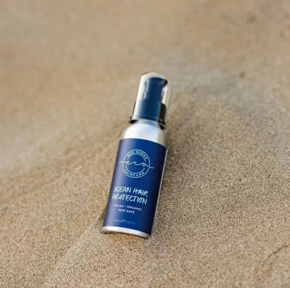 A blue bottle of beach hair protection serum by Evercircle laying on sand.